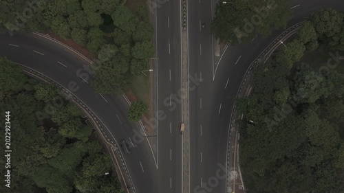 Top down aerial view of highway split with vehicles driving through lush green trees on asphalt road