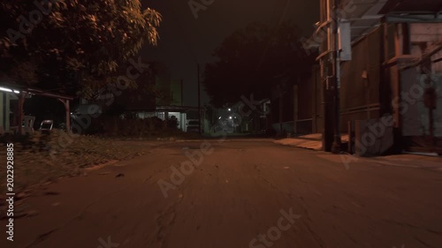Low angle driving shot through a dark empty suburban street at night under warm dim orange lamplight