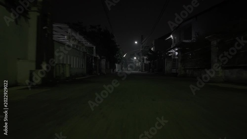 Empty suburban neighborhood street at night with dim streetlights and quiet residential houses