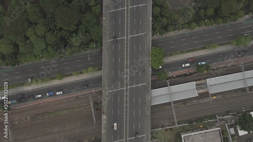 Top down aerial view of a flyover highway crossing over a railway station with moving vehicle traffic in Jakarta