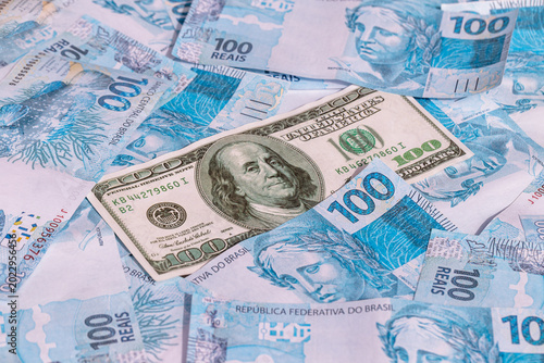 One hundred American dollar bill, stuck between 100 Brazilian real bills. Economic crisis and drop in the American currency