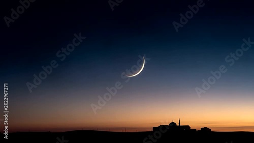 Crescent moon rises over silhouette of distant mosque