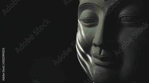 The face of the Buddha statue in the darkness is illuminated by a flickering light