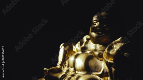 A golden smiling Buddha statue illuminated by a flickering light in the darkness
