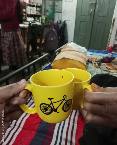 two yellow mugs with bicycle design clinking together in cozy indoor setting