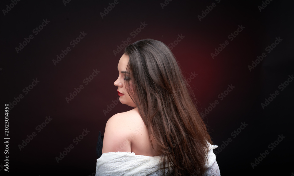 Naklejka premium A young woman poses in a white lace blouse on a dark blue background. The shirt is unbuttoned and her beautiful breasts are visible.