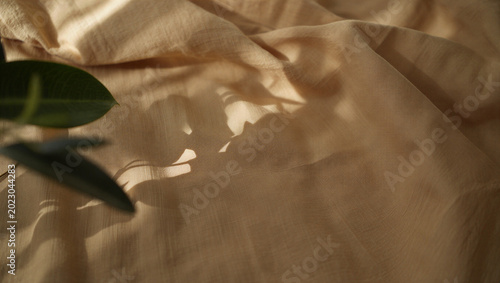 Billede på lærred Soft shadows of plant leaves on draped beige textile fabric background