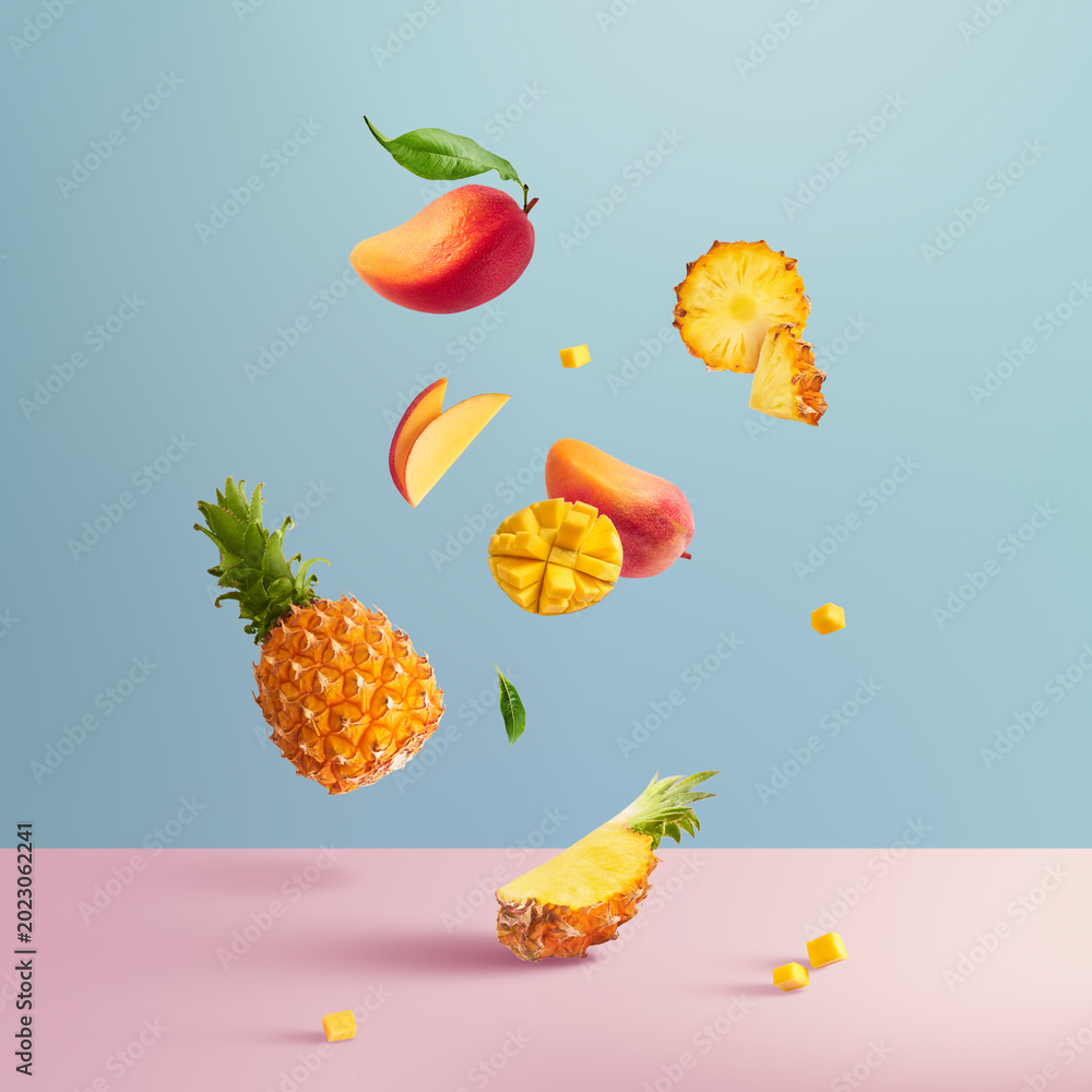 Fototapeta premium Levitating fresh tropical fruits. Sliced and whole pineapple and mango falling in the air on blue and pink background. Creative dynamic summer food composition.