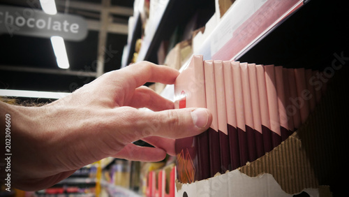 фотографія A buyer's hand taking a chocolate bar from a retail display close-up