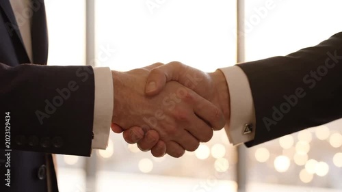 Close up of two businessmen shaking hands in a formal setting against a blurred bright window background