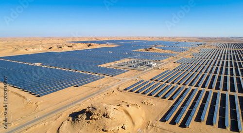Aerial drone view of a massive solar panel farm generating renewable energy in a desert landscape under a bright clear blue sky