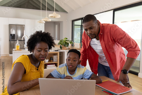 Photos African American family leaning over laptop with notebooks at dining table in ki