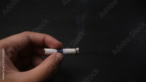 Bild auf Leinwand Close-up of a hand holding a burning cigarette with smoke on a dark background