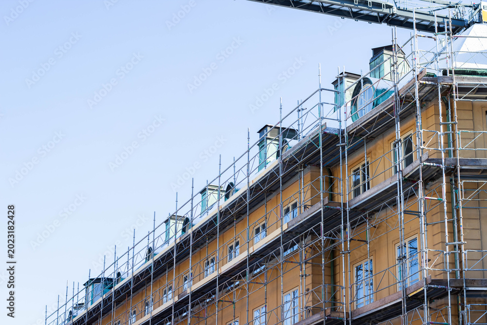 Fototapeta premium Building under construction with scaffolding and cranes, showcasing a multi-story structure with windows and a clear blue sky in the background