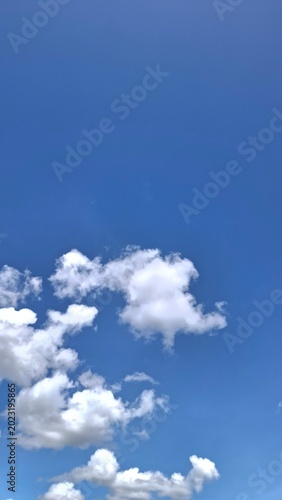 Fluffy white clouds on a bright blue sky, clear sunny day atmosphere, vertical natural background for copy space.