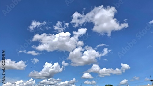 Fluffy white clouds on a bright blue sky, clear sunny day atmosphere, vertical natural background for copy space.