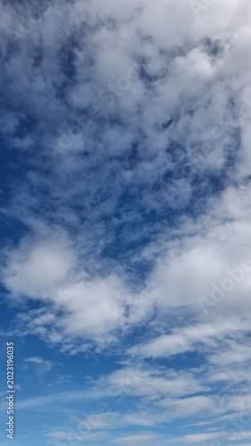 Fluffy white clouds on a bright blue sky, clear sunny day atmosphere, vertical natural background for copy space.