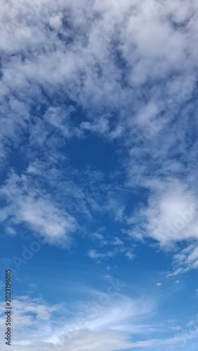Fluffy white clouds on a bright blue sky, clear sunny day atmosphere, vertical natural background for copy space.