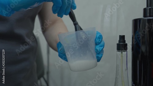 The master of creating hairstyles in a plastic container mixes a hair product and a hairstyle.