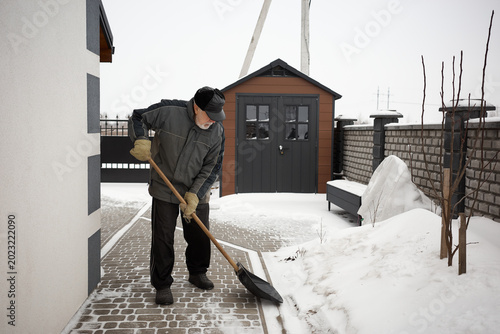 Senior man shovels snow from walkway near home in winter morning