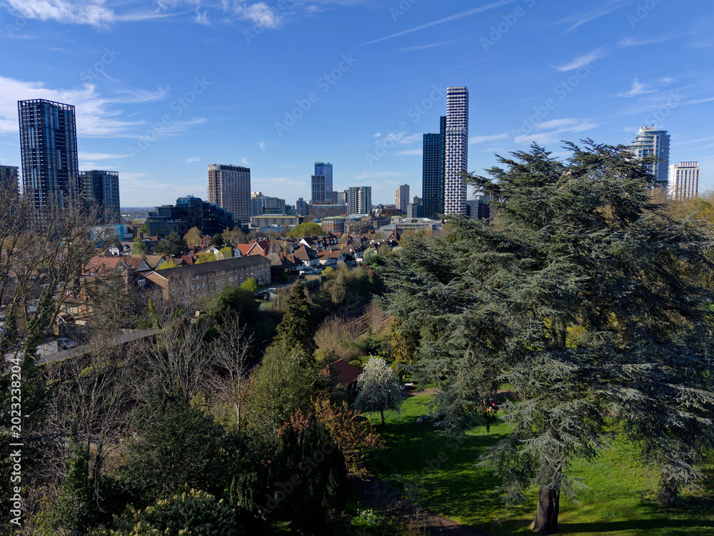 Fototapeta premium Modern Croydon skyline with tall skyscrapers in Greater London. Aerial view towards business district from Park Hill. Green trees with modern architecture in the background. Sunny day with blue sky.