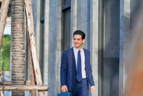 Businessman in formal navy suit walking on the street along the building office to work or meeting.