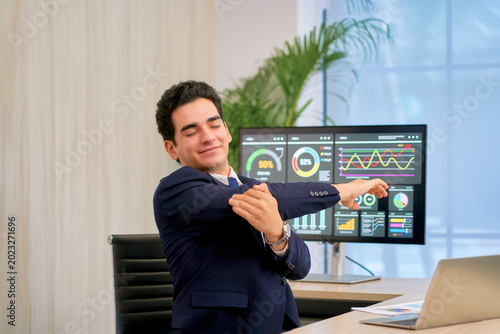 Businessman in navy suit stretch oneself on his desk office with monitor graphic information.