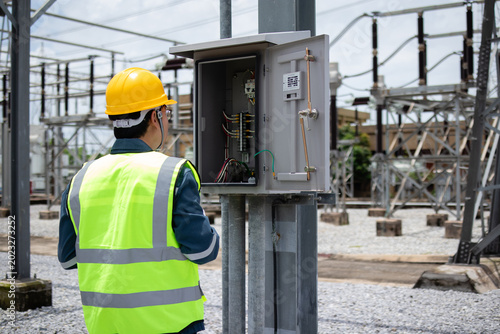 Cuadro en lienzo Engineer inspects an open outdoor electrical cabinet at a substation, checking wiring and control components for maintenance, safety, diagnostics, and grid reliability