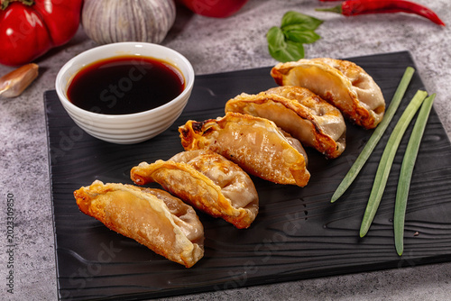 Fried gyoza dumplings on black plate with soy sauce and fresh vegetables