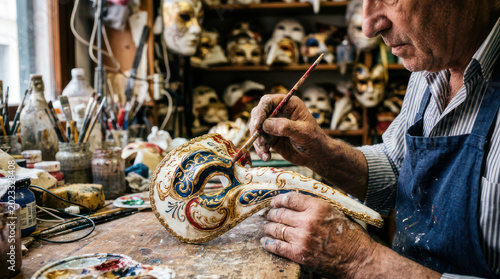 Craftsman meticulously painting a traditional Venetian mask with fine detail.