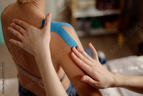 Close up of Caucasian adult woman receiving kinesiology taping on shoulder during physiotherapy, supporting pain relief and recovery. Useful for rehab, sports injury, wellness marketing