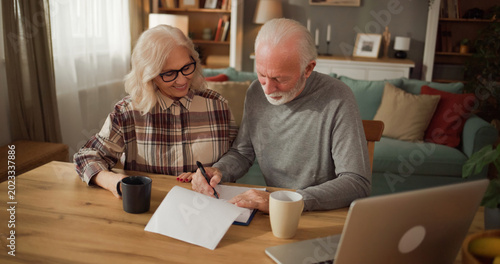A couple is engaged in a conversation about life insurance. They are sitting at a wooden table, reviewing documents, with coffee cups nearby. There is a laptop open on the table.