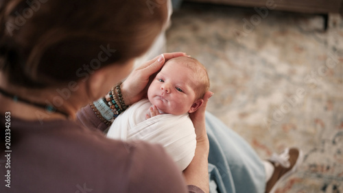 Mom Holds Newborn Baby In Warm Indoor Setting.