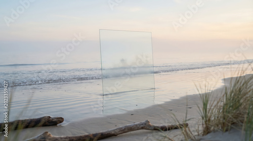 transparent glass panel standing on wet beach at sunset minimalist coastal reflection ocean waves sand dune grass abstract luxury calm interior design concept serene escapism nature horizon