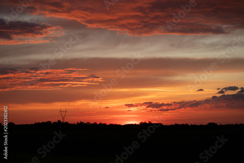 Spectacular red-orange clouds illuminated by the setting sun in the evening sky. The intense colors and dynamic cloud structure create a dramatic, picturesque atmospheric landscape.