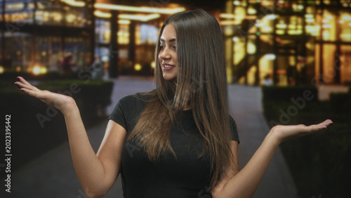 Foto Woman holding palms up and presenting with hands at a lit mall building entrance while smiling and looking at camera; confidence