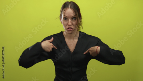Fotografie Young hispanic woman pointing to chest with both index fingers in lime green studio, open mouth and wide eyes; indignation disbelief