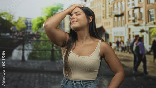 Konstfotografi Woman touching forehead with raised hand and closed eyes on a street beside a canal and buildings; relief travel memory