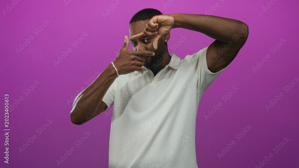 Naklejka premium Man framing face with fingers in posed studio against vibrant purple backdrop; creativity inspiration.