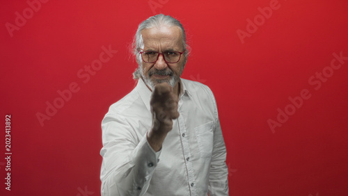 Photos Man with hoary long hair and beard points finger directly at camera in studio red backdrop; challenge confidence
