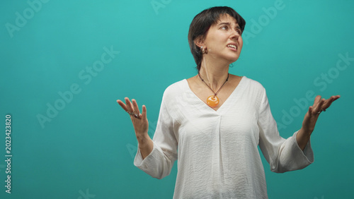Obraz na plátně Woman short hair wearing orange pendant necklace with hands raised and eyes closed in an expressive pleading gesture in studio; frustration
