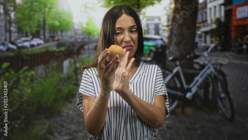 Konstfotografi Hispanic woman holding muffin pushes hand away on street near canal and bicycles in amsterdam; disgust rejection