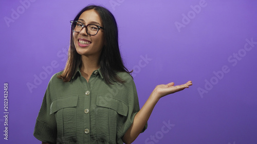 Foto Young brunette woman holding out hand in studio with purple background; happiness confidence warmth