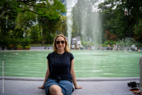 Woman in sunglasses relaxes by a fountain in a lush green city park