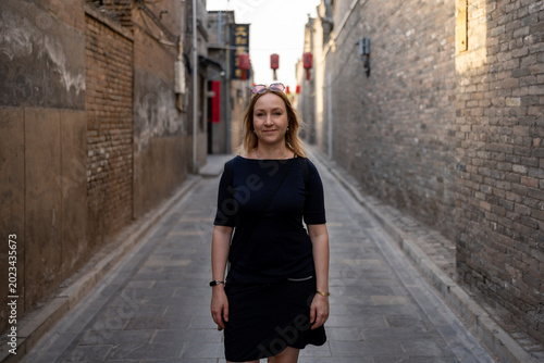 Woman walking down a narrow ancient street with brick buildings and red lanterns