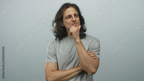 Tableau sur toile Young hispanic man with long hair hand on chin in studio with pale blue backdrop; thoughtful introspection reflection