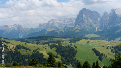 Expansive mountain landscape showcasing rolling hills and majestic peaks under a bright blue sky in the Alps