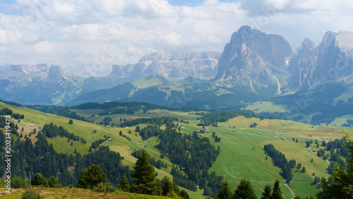 Breathtaking view of lush green valleys surrounded by majestic mountain peaks under a cloudy sky in the Dolomites during summer