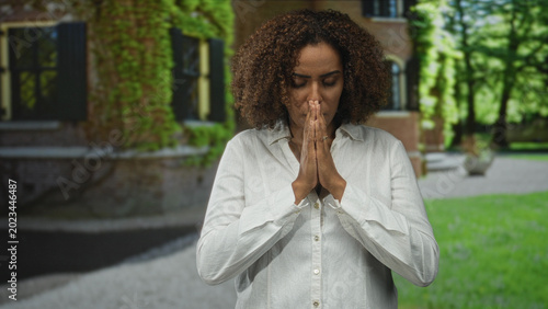 Tableau sur toile Woman praying with hands pressed together near face at building entrance outdoors; contemplation healing