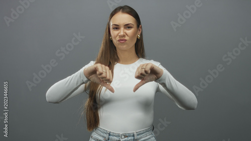 Foto Woman showing thumb down gesture with neutral expression and long hair in studio; disapproval rejection
